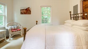 Un dormitorio con una cama grande, una silla de mimbre y una ventana con vistas a árboles.