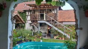 Una piscina con un pontile in legno, circondata da piante in vaso e un edificio rustico con un balcone.