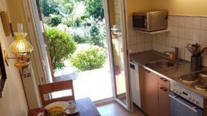 A small kitchen with a microwave, stove, and sink. There is a dining table with a plate, cup, and fruit. - Casa Elena by Interhome (Locarno Tegna)