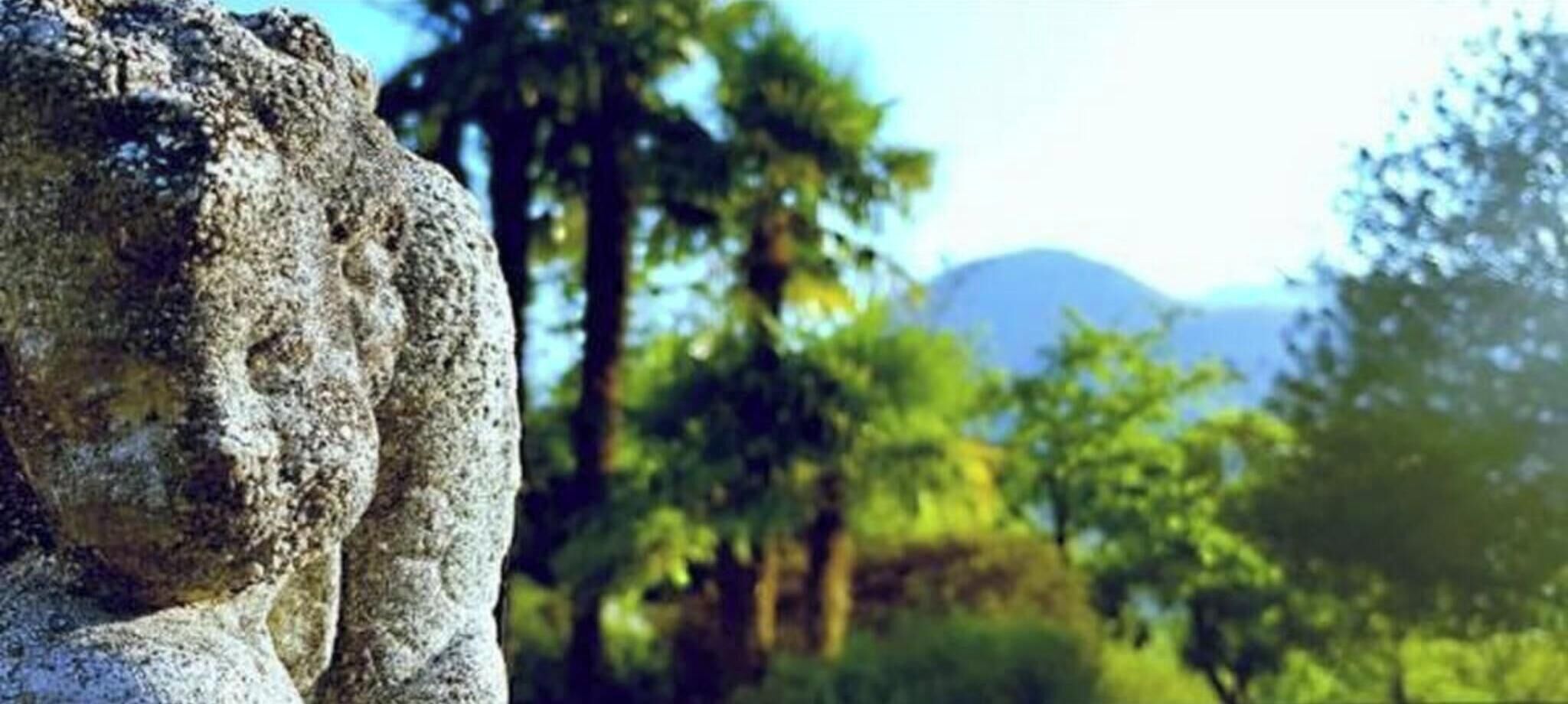 A stone statue in a natural setting with trees and mountains in the background.