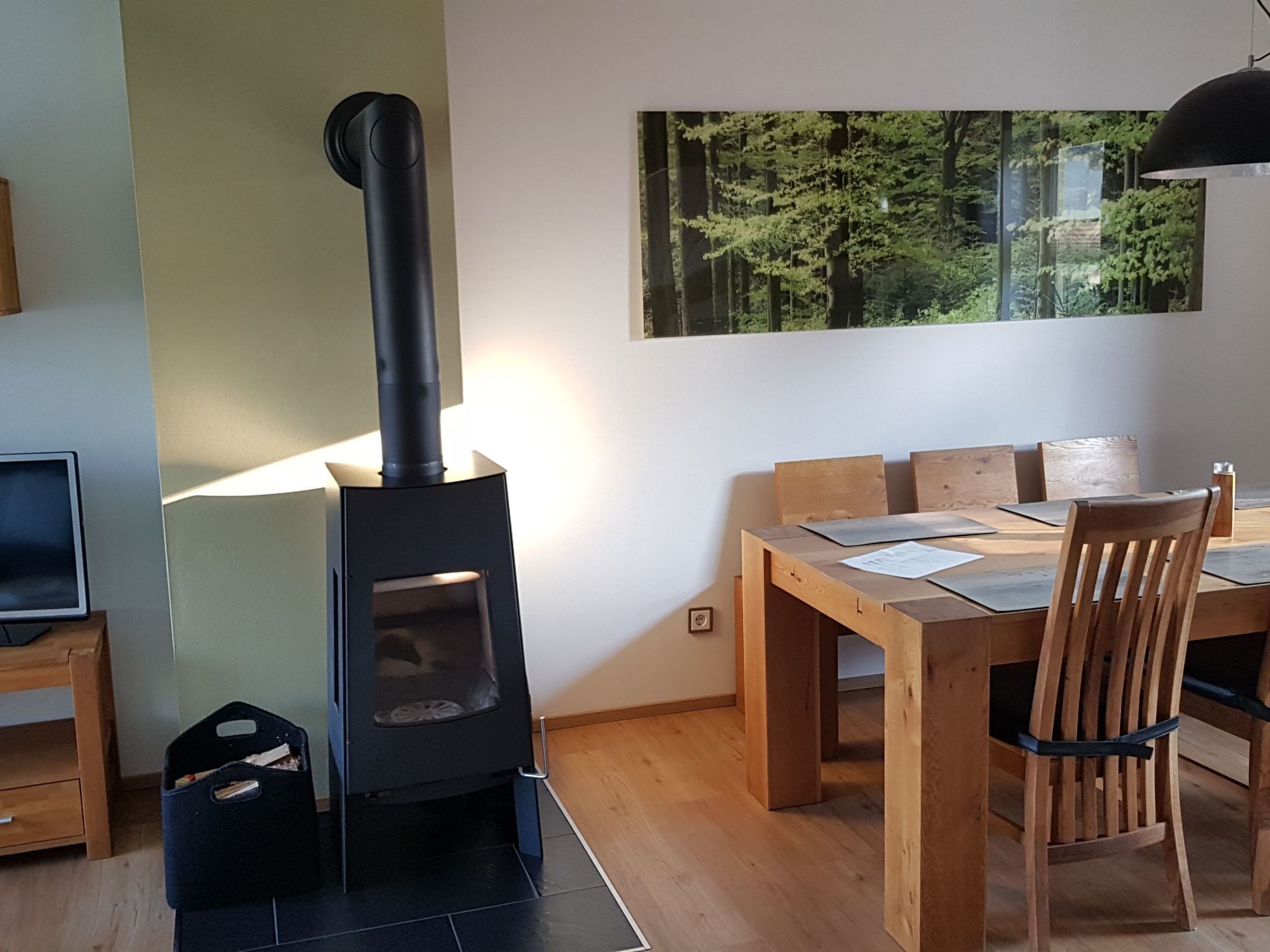 Una camera moderna con una stufa a legna in legno nero, un tavolo da pranzo con sedie e un'ampia finestra vista foresta.