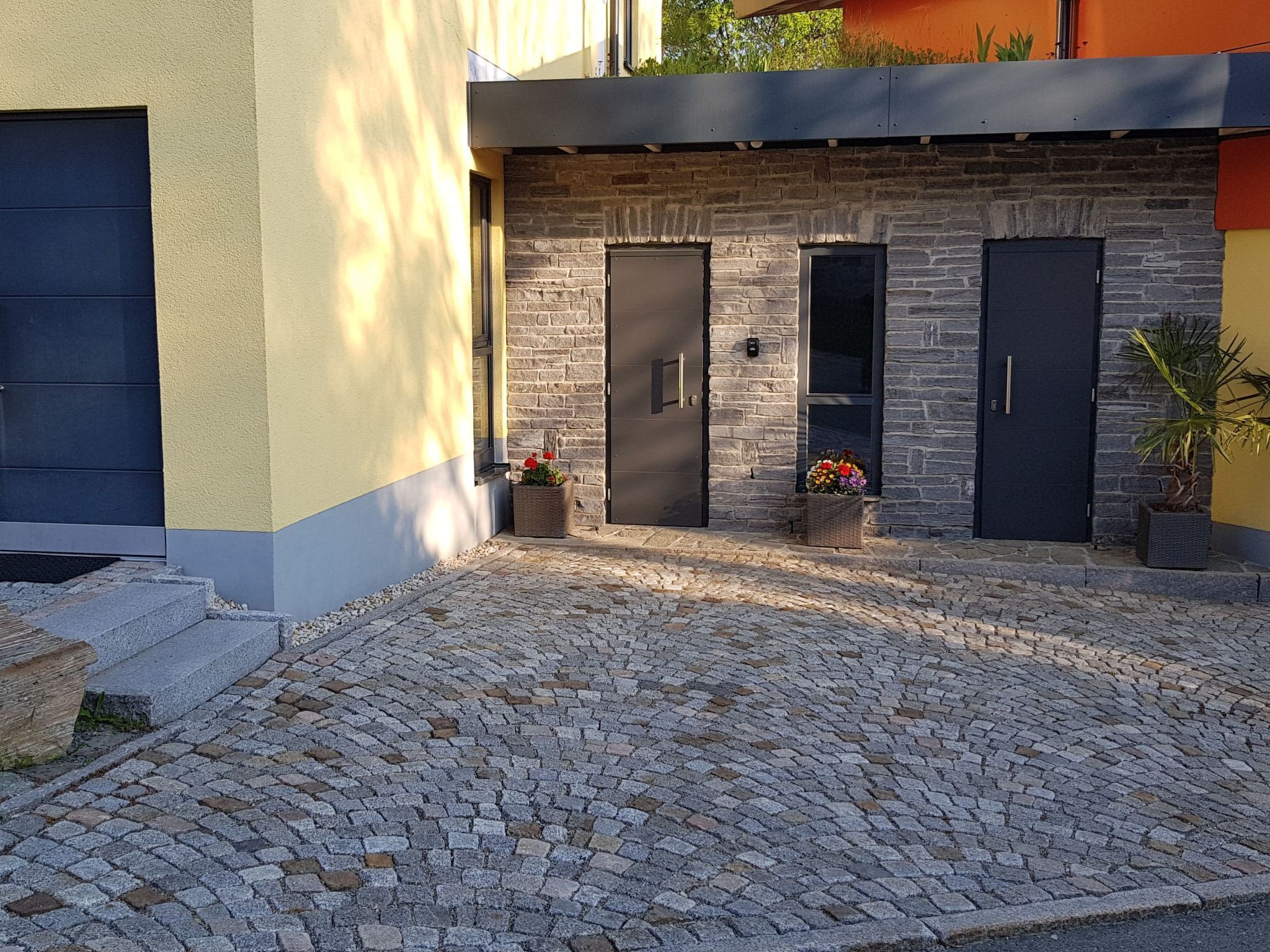 Un patio con pavimento de adoquines, un muro de piedra y dos puertas oscuras.