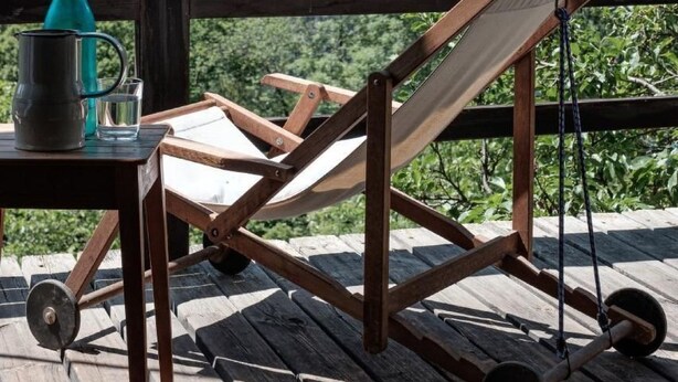 A wooden deck with a wooden chair and a table with a water bottle and glass. - La Stalla by Interhome (Faido)