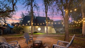 A backyard with a fire pit, Adirondack chairs, and string lights. - Montgomery Ranch | Stunning Lake House (Redding)