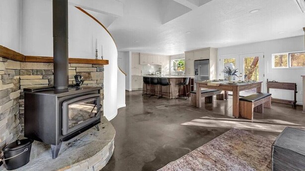 A spacious kitchen with a stone fireplace, a dining area with a wooden table and benches, and a kitchen island with bar stools. - Montgomery Ranch | Stunning Lake House (Redding)