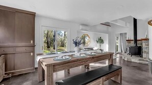 A modern kitchen with a large dining table, wooden cabinets, and a stone fireplace. - Montgomery Ranch | Stunning Lake House (Redding)