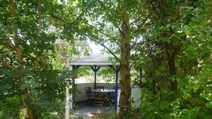A covered outdoor seating area with a table and chairs, surrounded by greenery and trees. - Haus-Zauberblau by Interhome (Groß Schoritz)