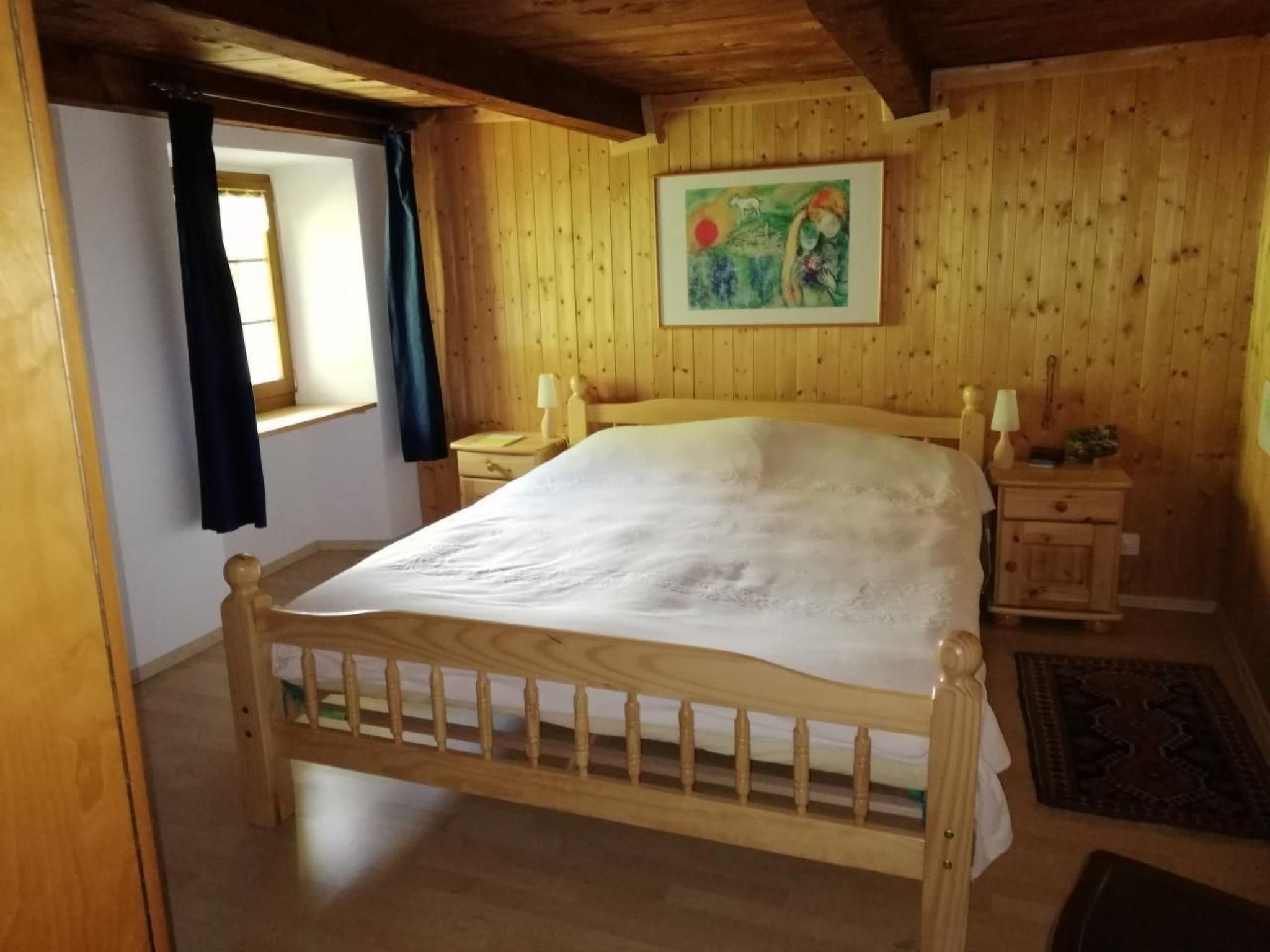 A wooden-framed bed in a room with wooden walls and a window with curtains.