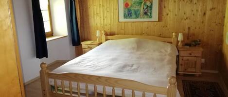 A wooden-framed bed in a room with wooden walls and a window with curtains.