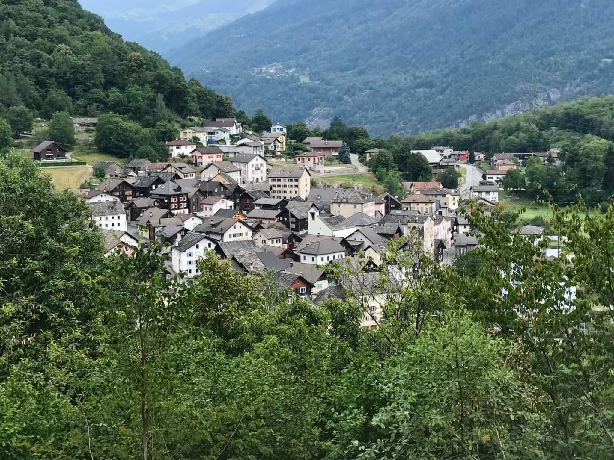 A hillside village with traditional buildings, surrounded by lush greenery and mountains in the background.