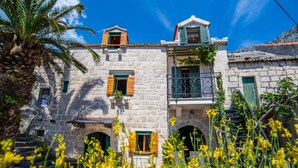 Un edificio de piedra con varias ventanas y balcones, rodeado de flores amarillas y una palmera.