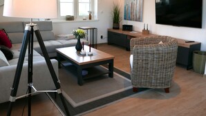 Uma sala de estar moderna com sofá, mesa de centro, luminária, poltrona de vime, televisão e um quadro na parede.