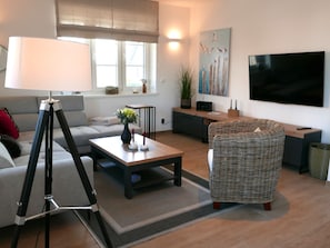 A modern living room with a sofa, a coffee table, a lamp, a wicker chair, a TV, and a painting on the wall. - Vacation home Knut by Interhome (Groß Schoritz)