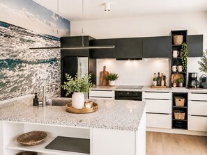 A modern kitchen with a central island, built-in appliances, and a large wave-themed mural on the wall. - Vacation home Knut by Interhome (Groß Schoritz)