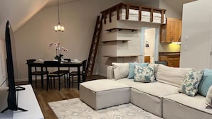 A modern living room with a sectional sofa, a dining table, and a kitchen area visible through an open door. - Peaceful Lakeside Apartment Garage & EV (Redding)