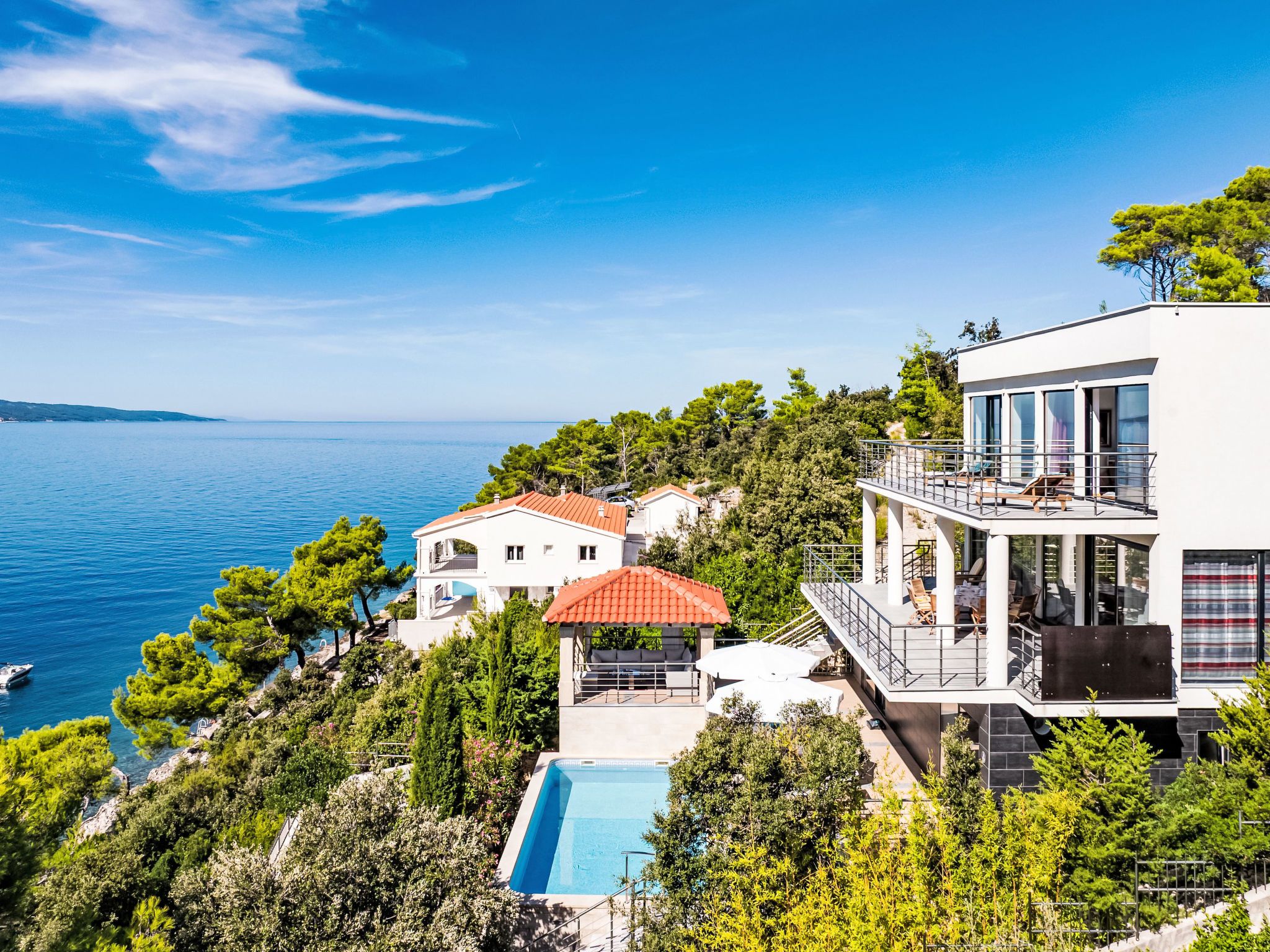 A coastal property with a pool, a red-roofed building, and a modern white building with a balcony.
