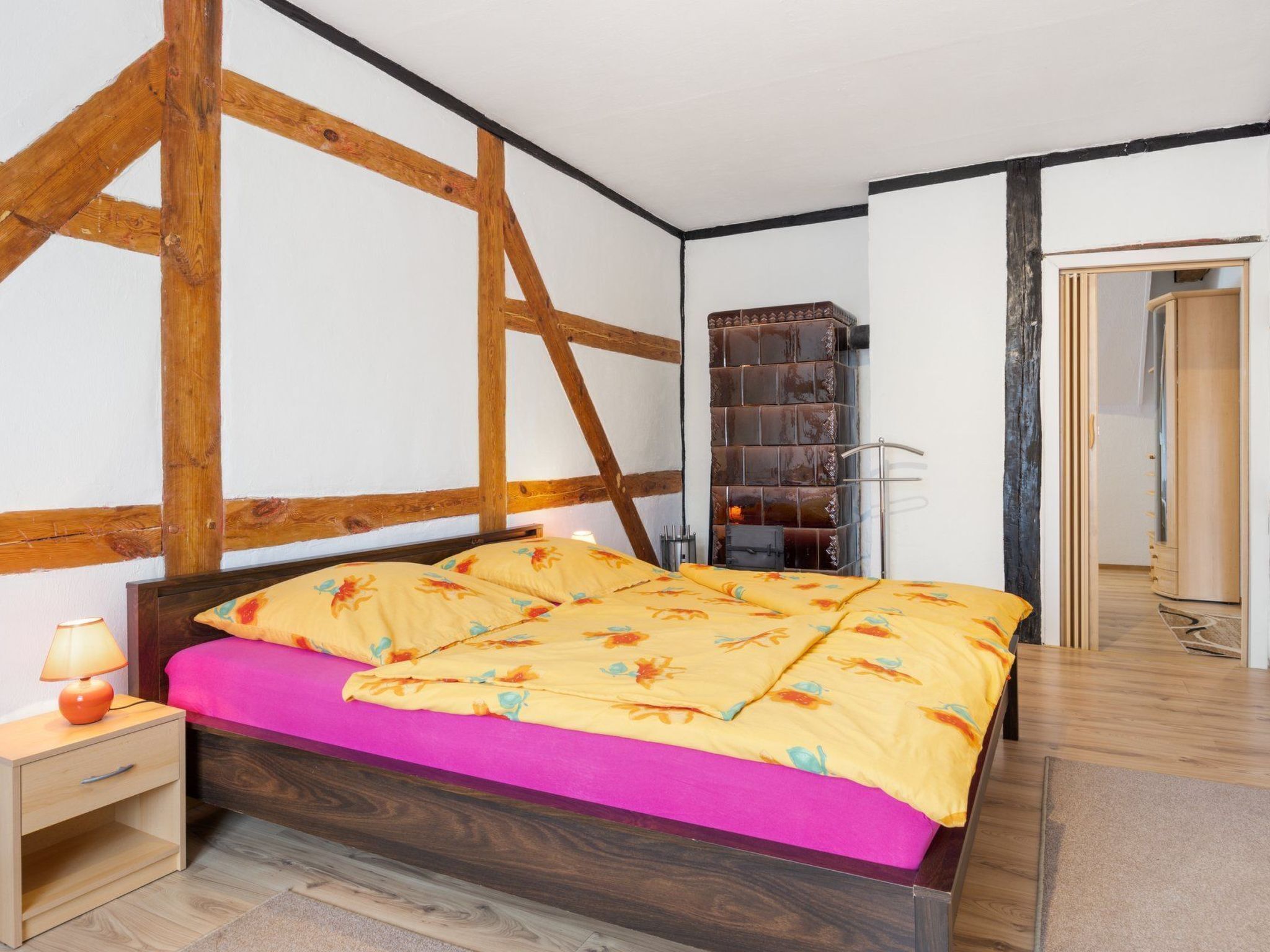 Une chambre à coucher avec un cadre de lit en bois, un matelas rose et une table de chevet en bois avec une lampe.