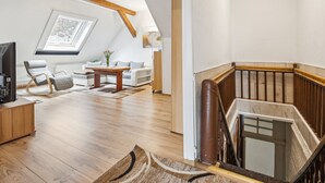 Un vaste espace de vie doté d’un haut plafond, de poutres apparentes, d’un escalier en bois et offrant une vue à travers une lucarne.
