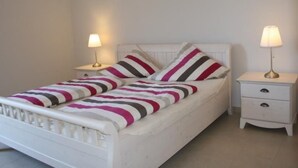 Quarto individual com uma cama de solteiro, cabeceira branca, duas mesas de cabeceira com luminárias e roupa de cama listrada.