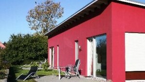 Um edifício vermelho com um alpendre, mesas ao ar livre e uma árvore ao fundo.