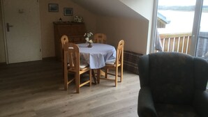 A dining area with a round table, wooden chairs, and a view of the outdoors through a large window.