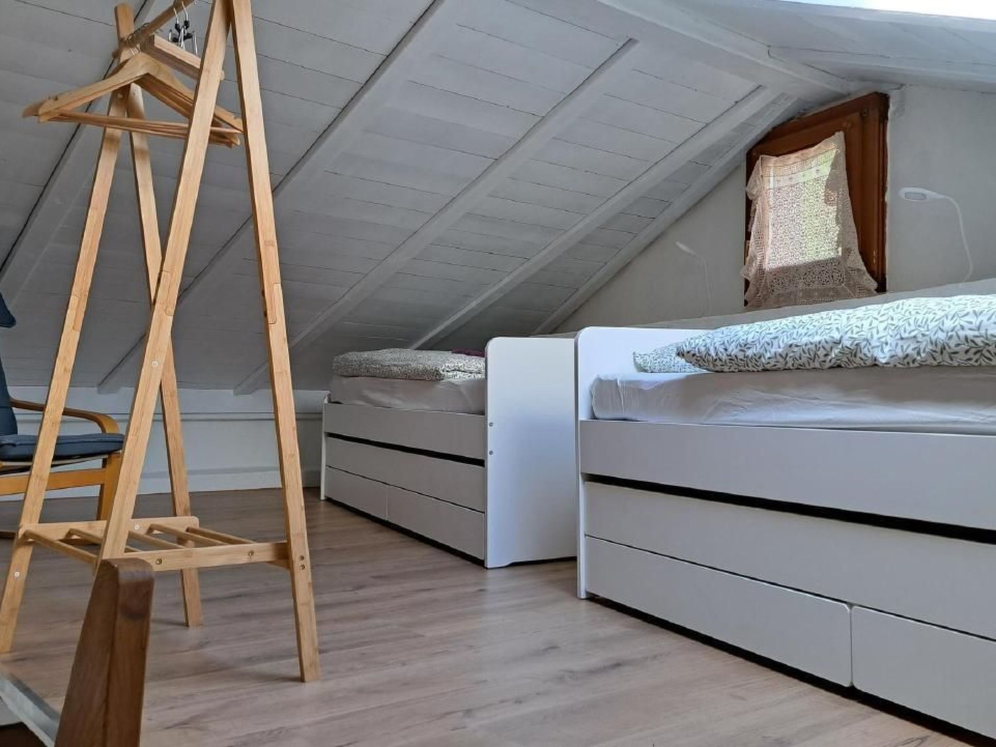 A loft bedroom with a sloped ceiling, a wooden ladder, a bed with a patterned bedspread, and built-in storage drawers.