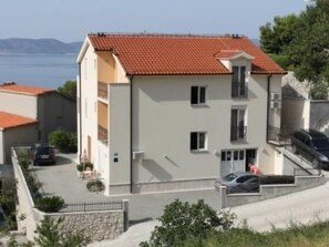 Ein zweistöckiges Gebäude mit rotem Ziegeldach, einem Balkon und einem Parkplatz mit Autos.