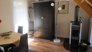Ein Essbereich mit Tisch und Stühlen, ein dunkler Holzschrank, eine Stehlampe und ein Kaminofen.