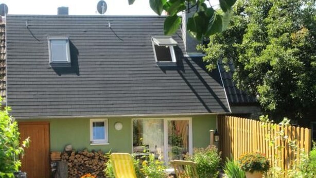 Ein Haus mit geneigtem Dach, einer kleinen Veranda und einem eingezäunten Garten.