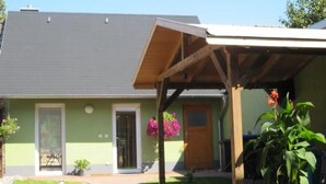 Ein Haus mit überdachter Veranda, grüner Fassade und einer Tür mit Fenster.