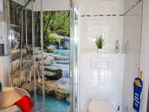A bathroom with a glass shower enclosure, a sink, a toilet, and a small shelf with toiletries. - Haus am Stein Haus 1 by Interhome (Königstein)