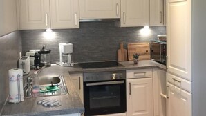 A modern kitchen with white cabinets, a built-in oven, a sink, and a coffee maker. - Apartment Anker by Interhome (Baabe)