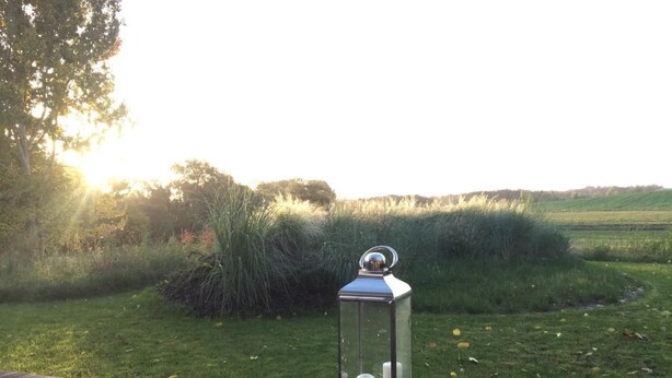 A wooden deck with a glass lantern containing candles, overlooking a grassy field with trees and a sunset in the background. - Apartment Anker by Interhome (Baabe)