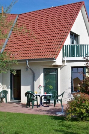 Una casa a due piani con tetto in tegole rosse, un balcone con ringhiere verdi e un piccolo patio con mobili da esterno.