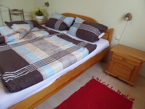 Un letto con copriletto e cuscini decorati, un comodino in legno, un tappeto rosso e un piccolo tavolino con una lampada.