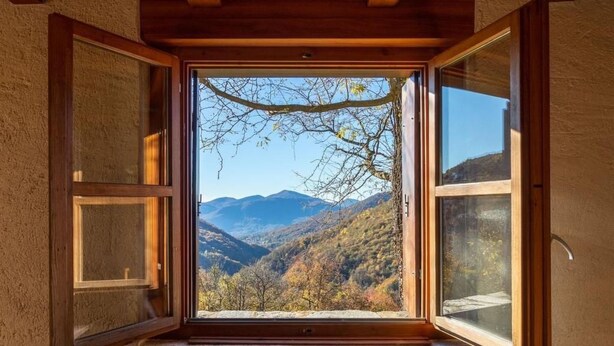 A room with a large window offering a view of mountains and autumn foliage. - Casa Chris by Interhome (Aranno)
