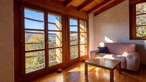 A cozy room with wooden floors, a sofa, and large windows offering a view of the outdoors. - Casa Chris by Interhome (Aranno)