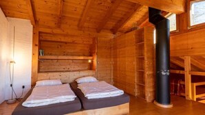 A wooden cabin room with two beds, a black chimney, and a window. - Casa Chris by Interhome (Aranno)