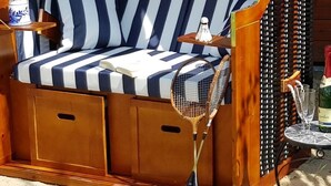 Una silla de playa a rayas con toldo, una botella de vino y una raqueta de tenis sobre arena.