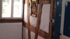 Una habitación con vigas de madera a la vista, un radiador blanco, un cuadro en la pared y una puerta azul.