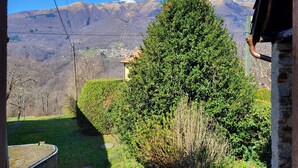 Ein Blick auf eine Berglandschaft mit einem großen Baum im Vordergrund und einem Gebäude mit geneigtem Dach im Hintergrund.