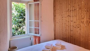 Ein Schlafzimmer mit Holzwand, einem Fenster mit Vorhängen, einem Bett mit Handtüchern und einem Korbwäschekorb.