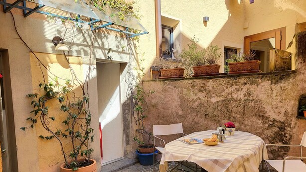 Eine gemütliche Terrasse im Freien mit einem Tisch für zwei Personen, umgeben von Kübelpflanzen und einer rustikalen Mauer.