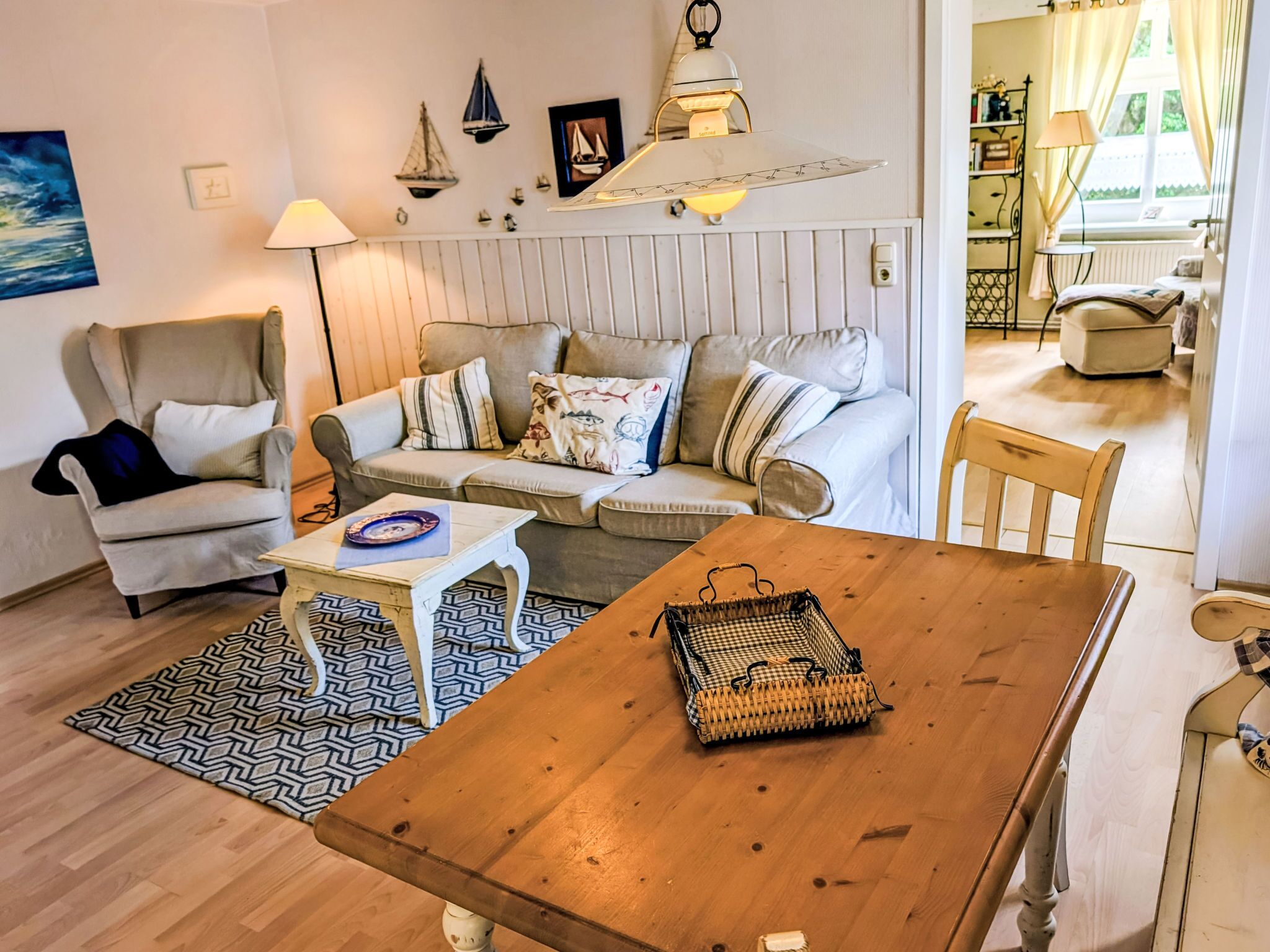 A cozy living room with a sofa, armchair, wooden table, and a dining area.