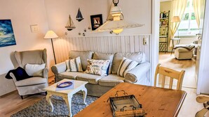 A cozy living room with a sofa, armchair, wooden table, and a dining area. - Apartment 45 qm by Interhome (Ahrenshoop)