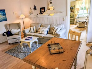 A cozy living room with a sofa, armchair, wooden table, and a dining area. - Apartment 45 qm by Interhome (Ahrenshoop)
