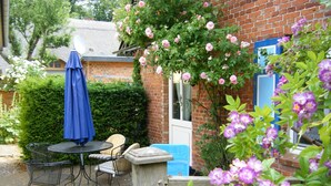 A patio with a round table and chairs, a blue umbrella, and a brick wall. - Apartment 45 qm by Interhome (Ahrenshoop)