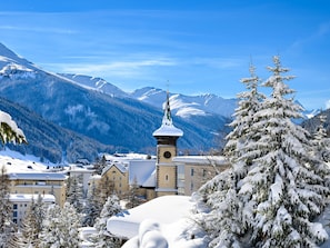 Une ville de montagne enneigée, avec un clocher d’église, des bâtiments et des arbres couverts de neige.
