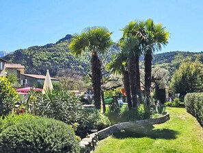A garden with palm trees, a stone wall, and a mountain in the background. - "Villa romaga mit Wallbox by Interhome (Vernet Les Bains)