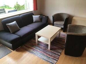 Un salon avec un canapé de couleur foncée, une table basse blanche, un tapis à motifs et un fauteuil noir.